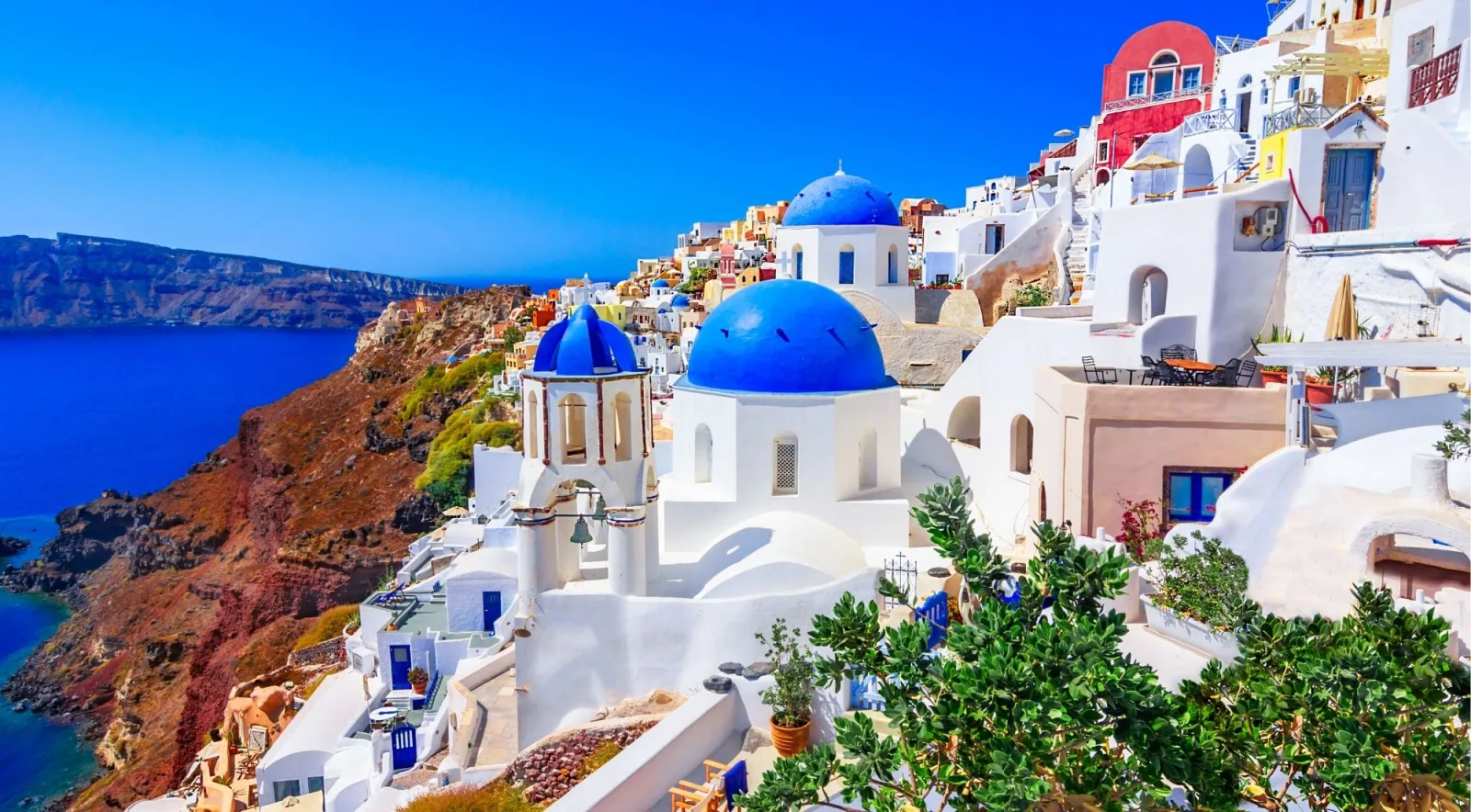 Blue-domed churches and whitewashed houses stepping down the caldera cliff at Oia, Santorini, above the deep blue Aegean