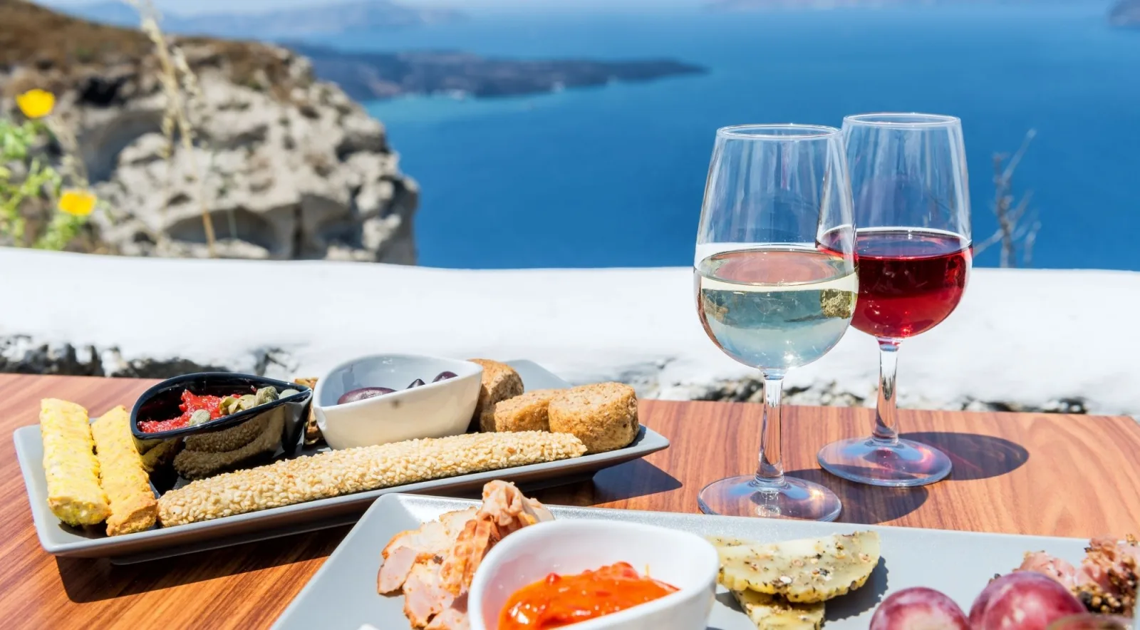 Glasses of white and rosé wine with a meze plate on a whitewashed terrace wall above the Santorini caldera and the Aegean