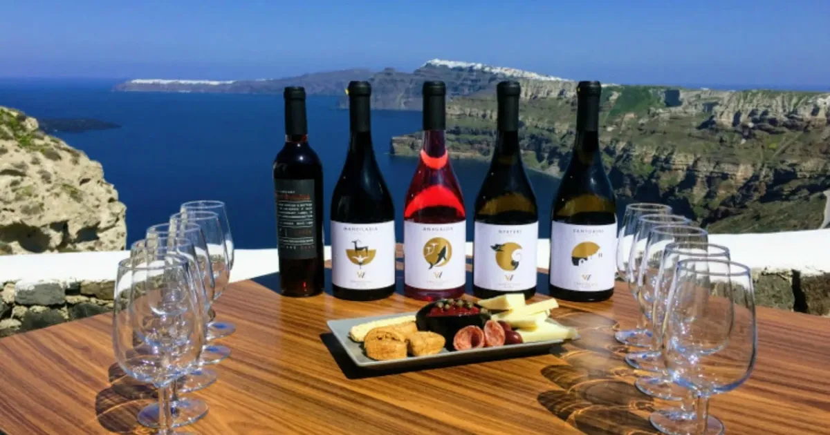 Bottles of Santorini, Nykteri, rosé and red wine lined up with tasting glasses and a meze plate on a terrace above the caldera
