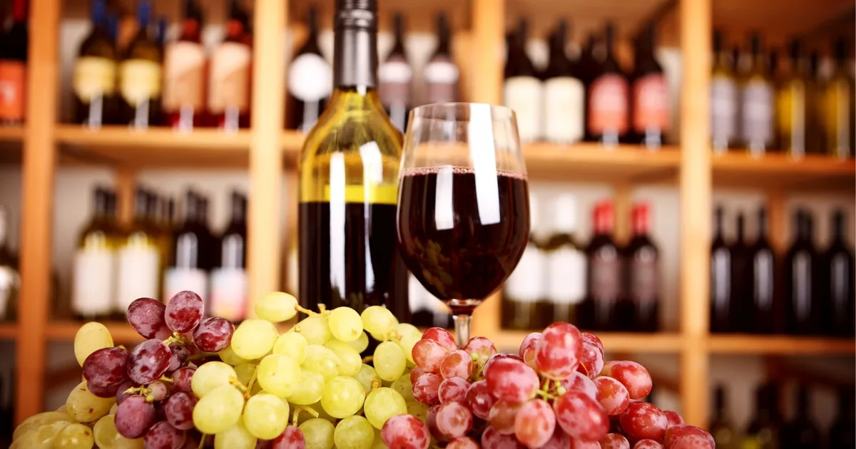 Wine bottles and a bunch of grapes on a wooden shelf, evoking the cellar setting of the Koutsoyannopoulos Wine Museum in Santorini